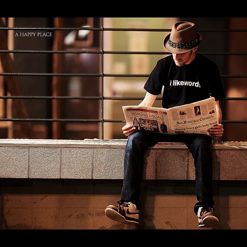 A man seated on a ledge, engrossed in reading a newspaper, with a serene backdrop enhancing the moment.