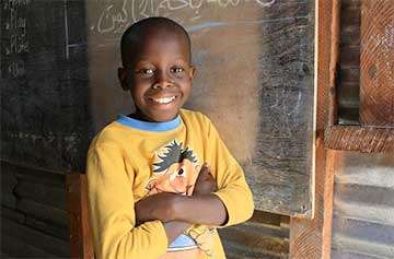 Smiling child in a classroom wearing a yellow shirt, representing confidence in English pronunciation.